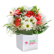 With its buoyant palette and joyful energy, this bouquet could only belong to Kingsbury-a place where neighbours gather and each season brings new colour to local gardens. The arrangement rises from a stylish white carrier bag, blooming with plush coral, peach, and bright red carnations whose delicately frilled petals invite touch. Lively white daisies, each with a fresh green-yellow center, offer brightness and good cheer, reminiscent of the spirit found at Kingsbury's bustling markets. Wisps of baby's breath weave throughout, softening the bouquet like morning dew. A frame of glossy, emerald-green foliage cradles the blooms and adds richness, while a scattering of closed buds tinged with gentle purple suggests the anticipation of new joy soon to blossom. Everything is artfully gathered into a full, rounded shape that hints at skilled local hands and plenty of care. Against the clean white setting, every detail-colour, shine, texture-stands out, making this bouquet the perfect gift for a Kingsbury birthday, an impromptu celebration, or a thoughtful delivery to someone special. Its understated presentation and elegant form capture the heartfelt pride and neighbourly warmth that define the local florist scene.